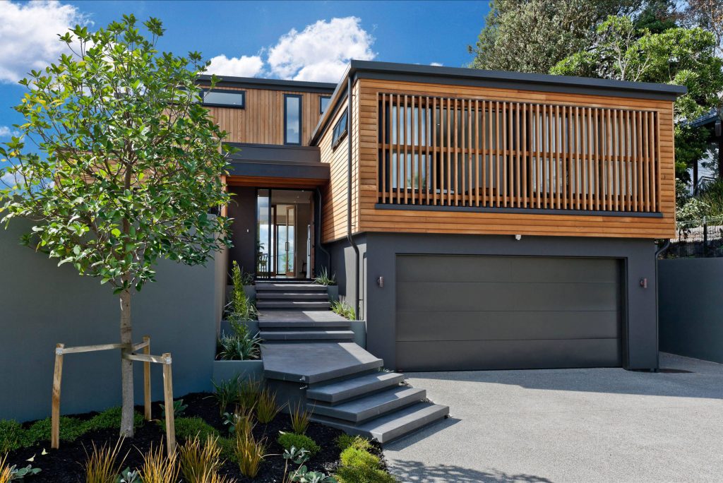 Modern grey garage door with concrete driveway and landscaped garden in front.