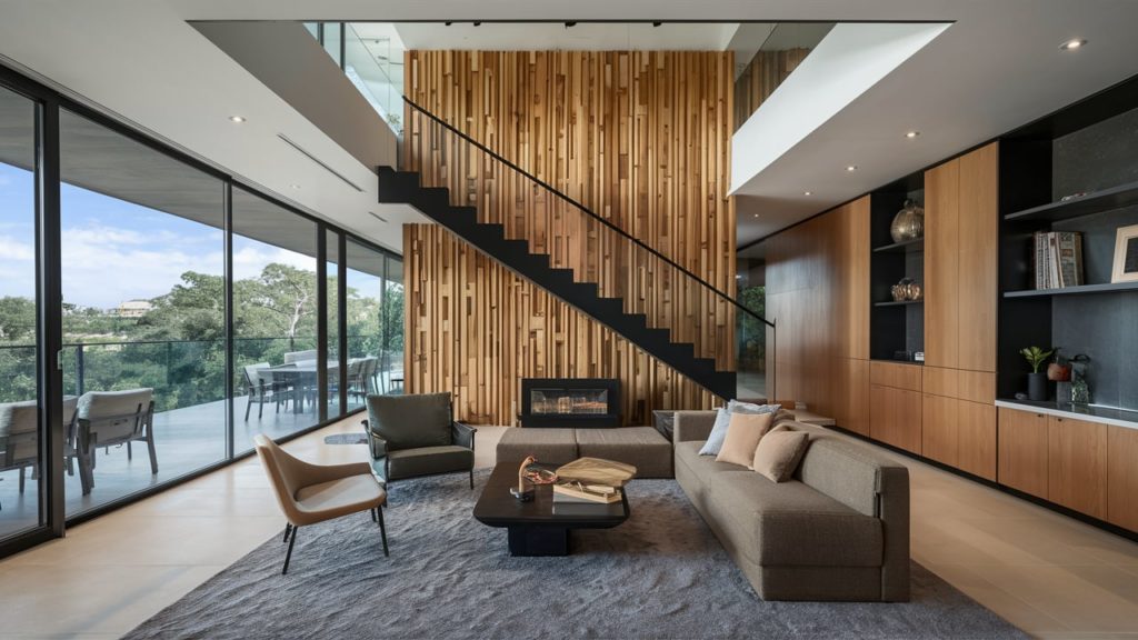 Modern living room featuring a cantilevered staircase with a wood wall paneling and large windows overlooking a balcony.