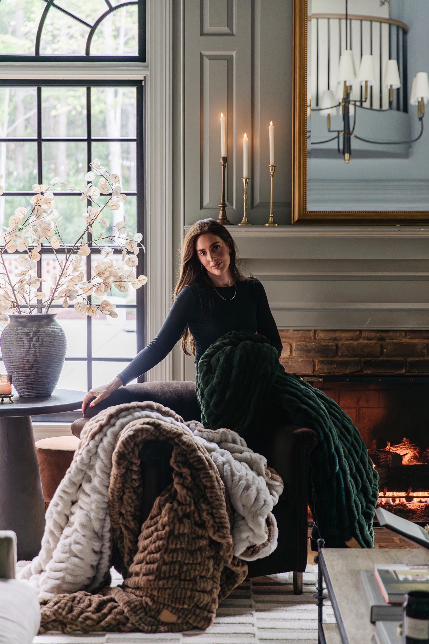 Chris Loves Julia | Julia perched on the side of a chair in the living room with CLJ x Lola Blankets in colors Corduroy, A La Mode, and Juniper