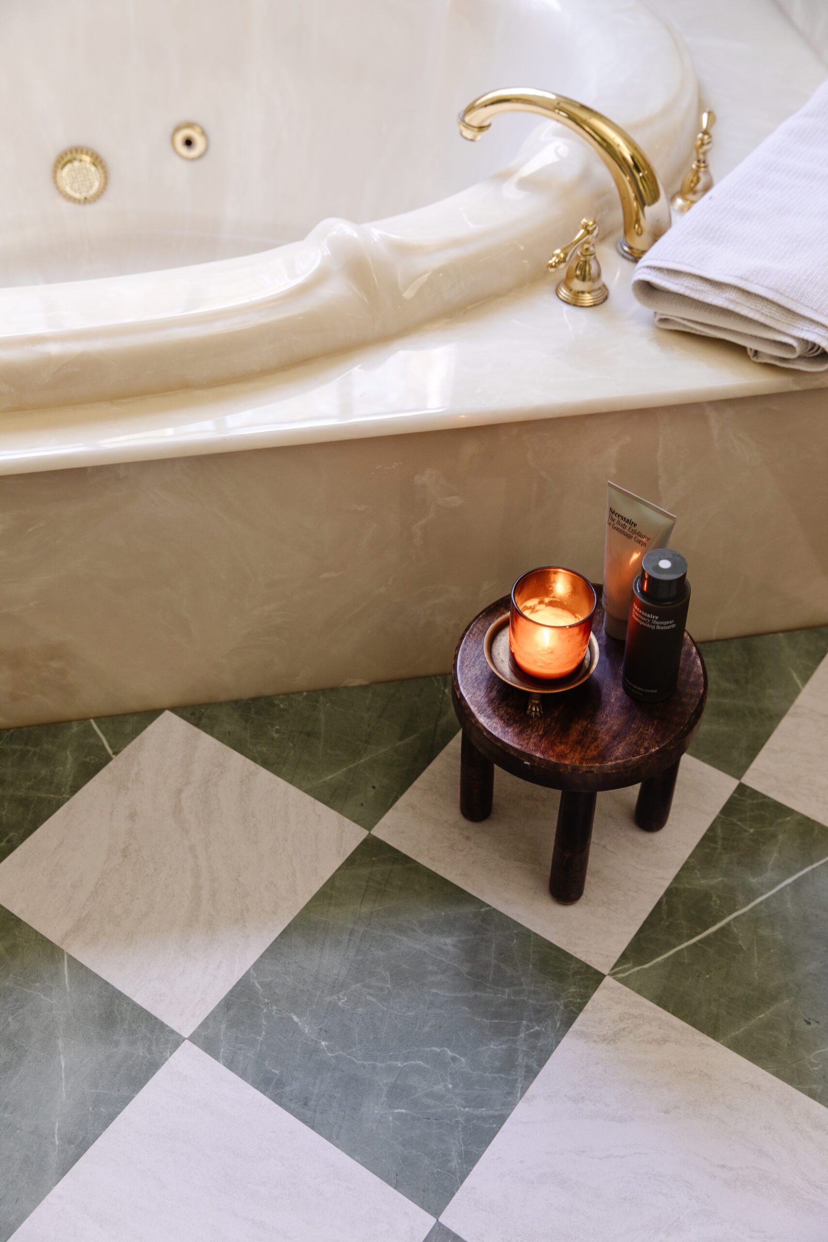 Close-up of a primary bathroom floor next to a tub featuring FloorPops peel-and-stick floor tiles in green & white marble checkerboard