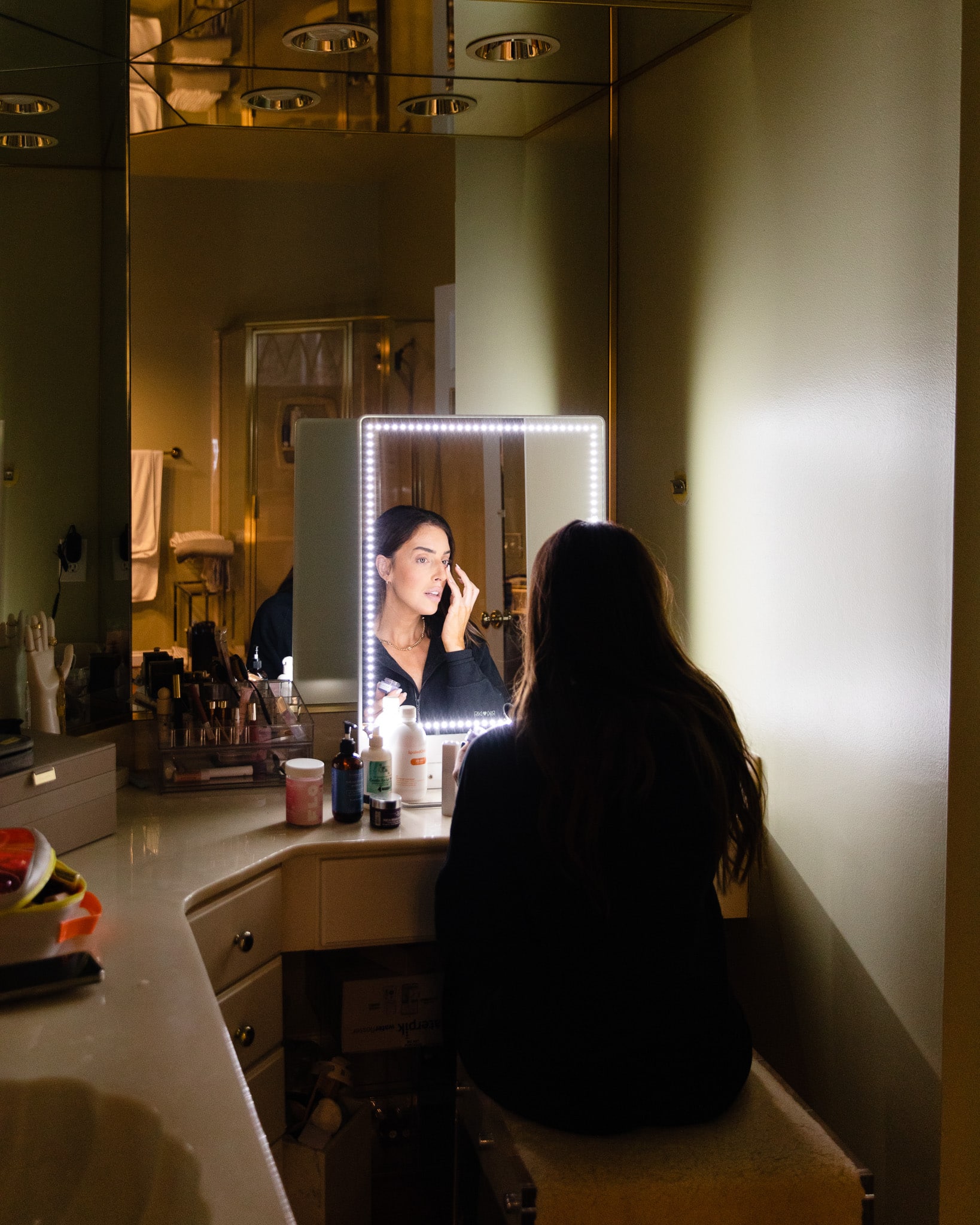 Julia sitting at the bathroom vanity applying makeup