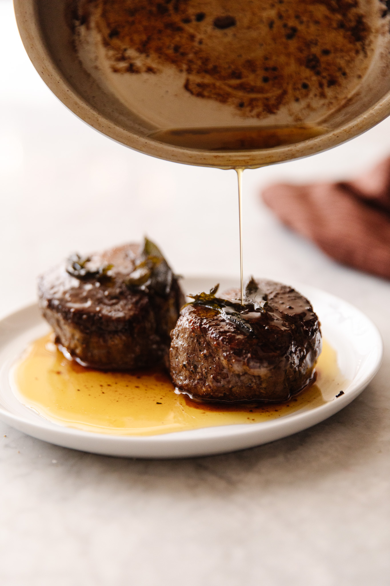 A pan pouring ghee (liquid gold) over two perfectly cooked filet mignon steaks