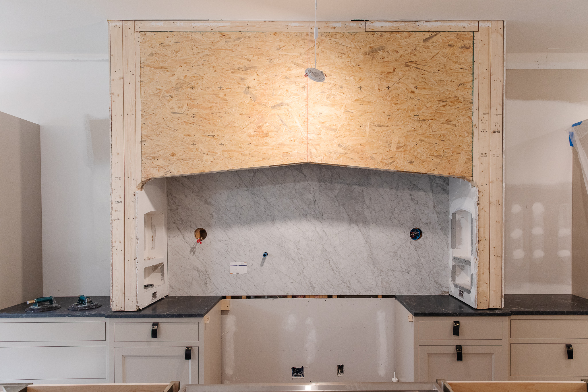 The installation of the range hood and marble backsplash in the range nook