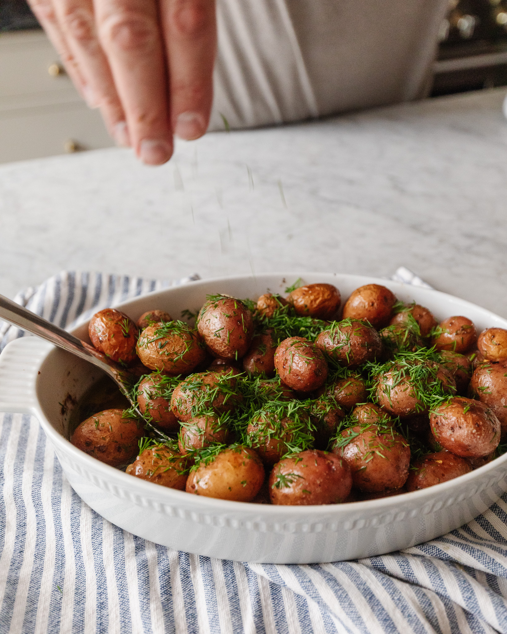 Hand sprinkling fresh chopped dill over roasted red potatoes