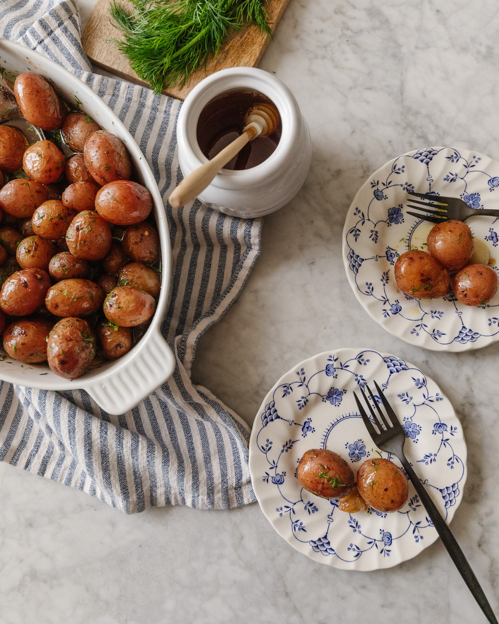 Two white and blue side plates showing baby red potatoes with dill & honey glaze
