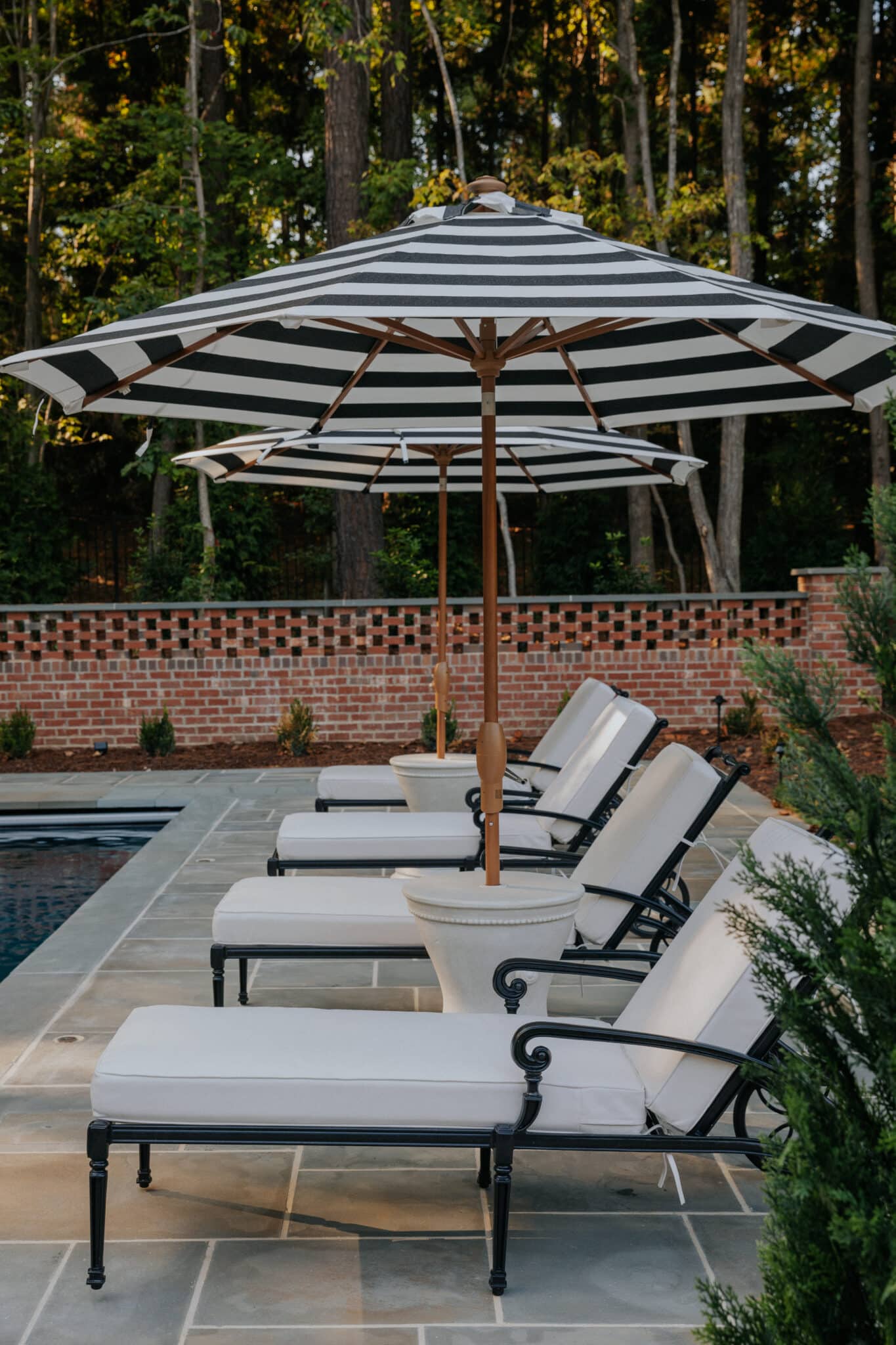 Black-and-white market-striped patio umbrellas over poolside chaise lounge chairs