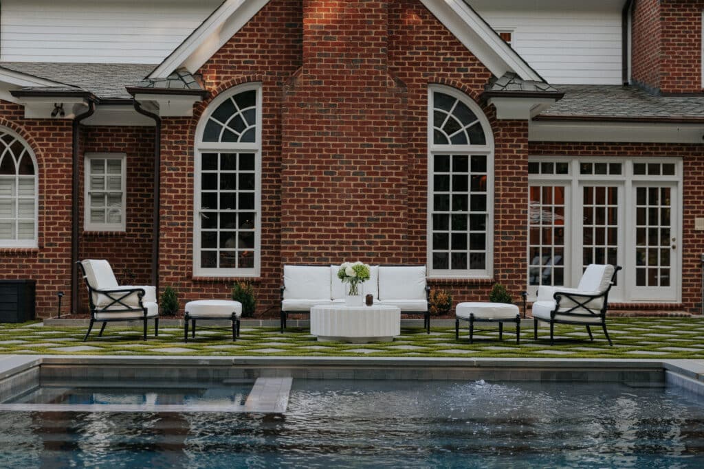 White-cushioned iron wrought furniture including a white and black outdoor sofa and two outdoor chairs and ottomans on a back patio