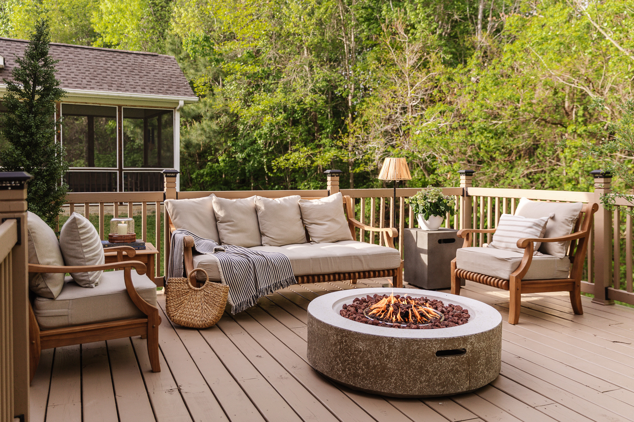 A cozy outdoor sitting area with outdoor sofa and two side chairs around a fire table on a deck
