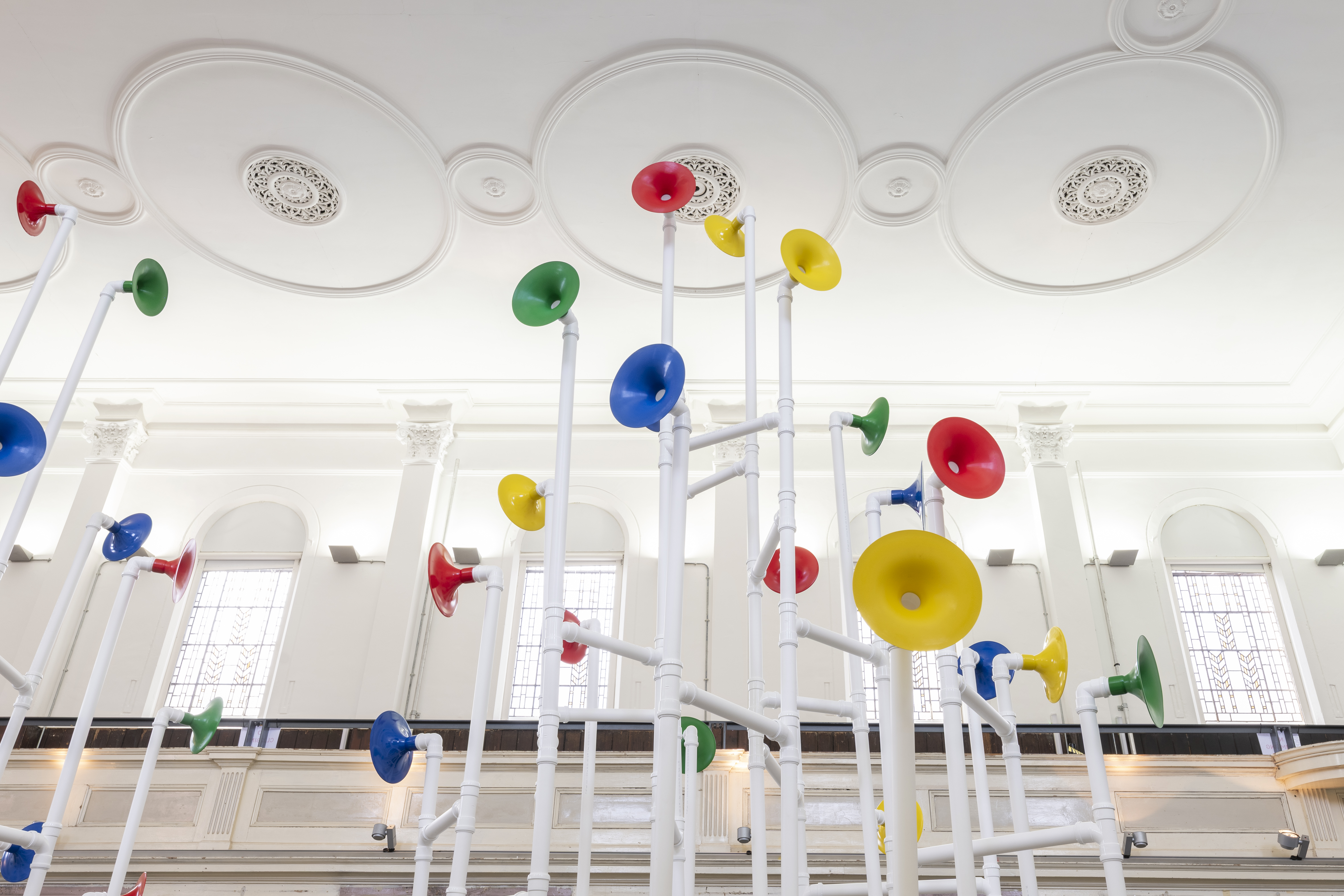Installation in a former church made out of white pipes and colourful funnels