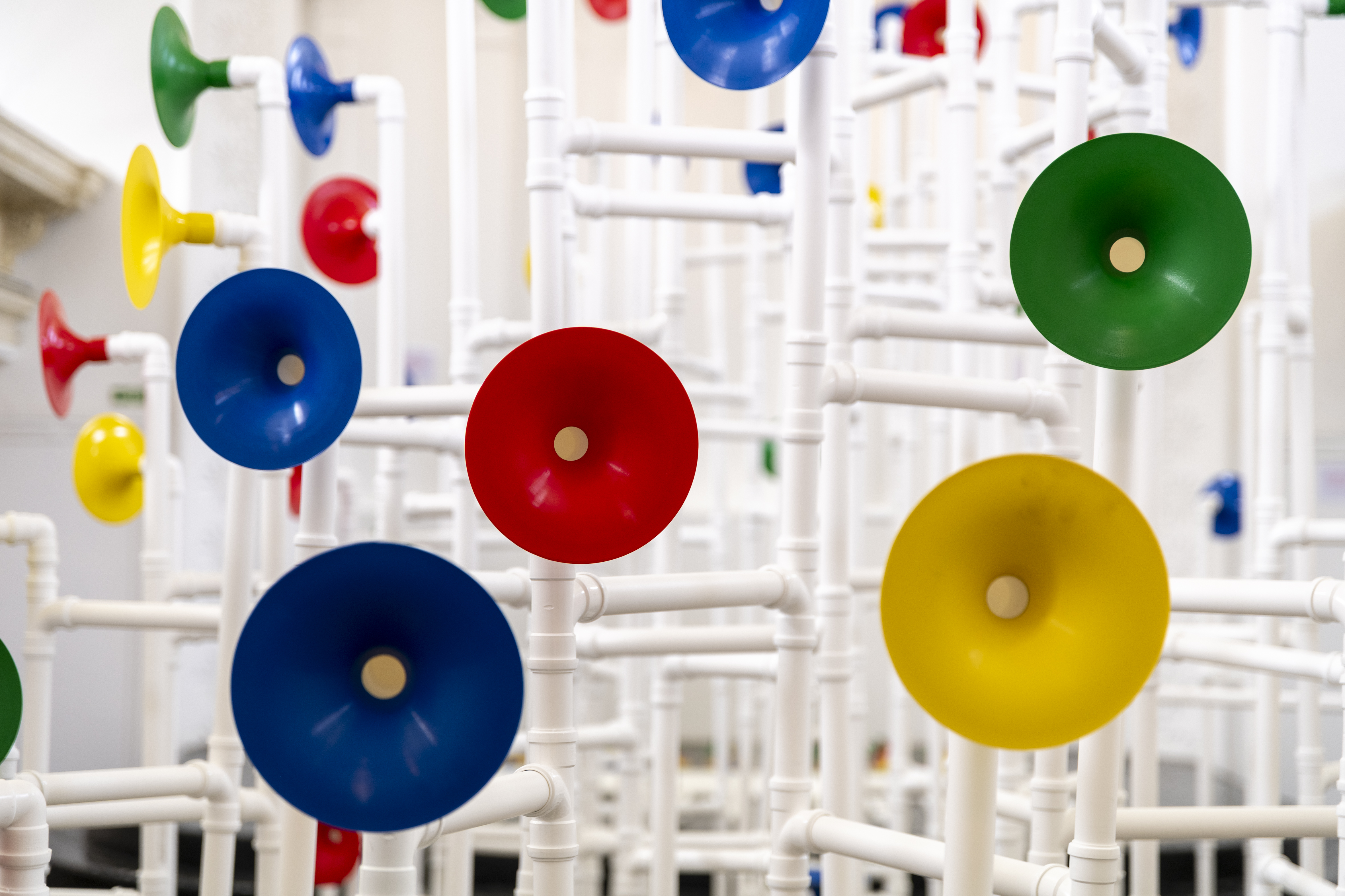 Installation in a former church made out of white pipes and colourful funnels