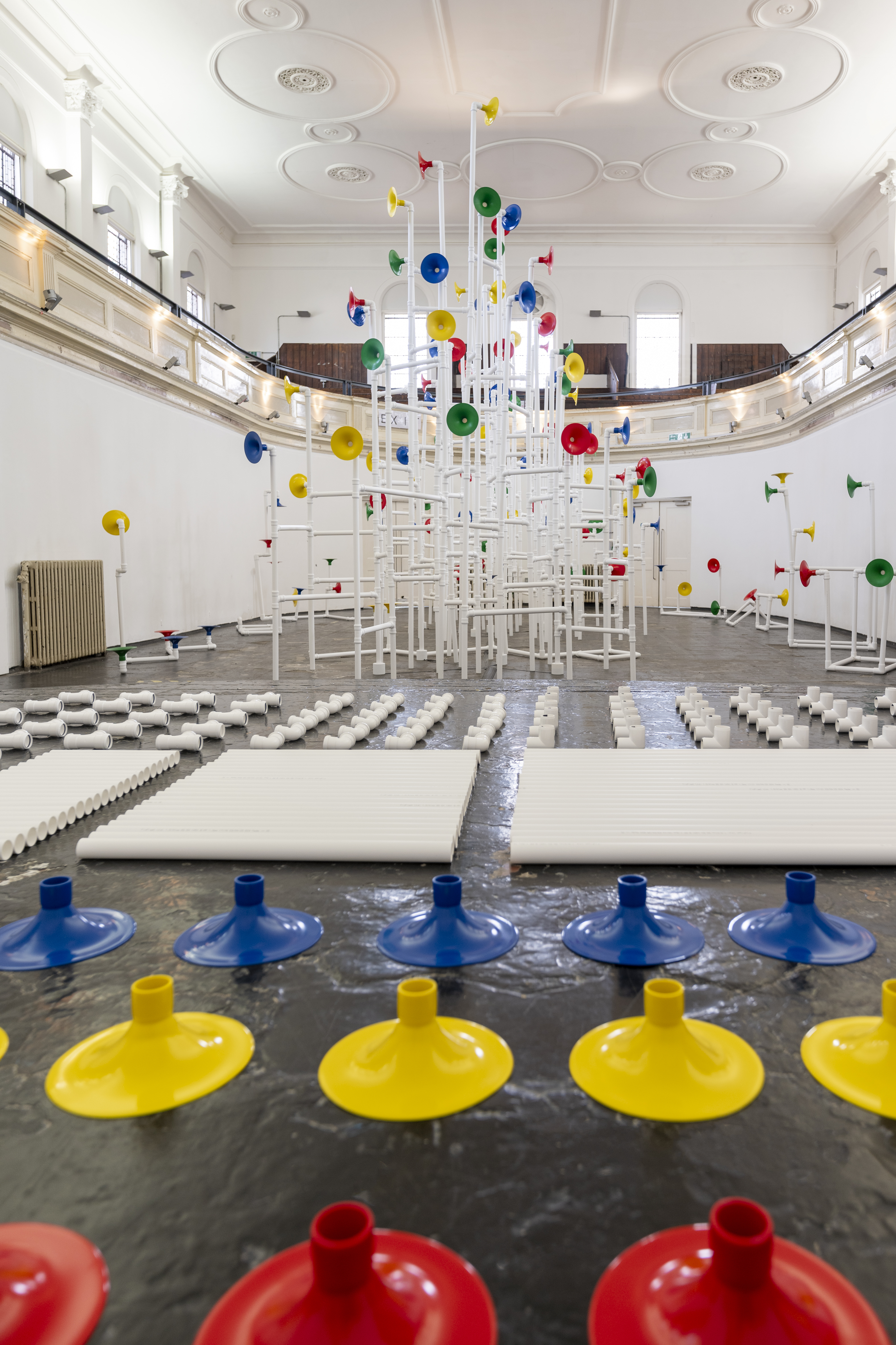 Installation in a former church made out of white pipes and colourful funnels