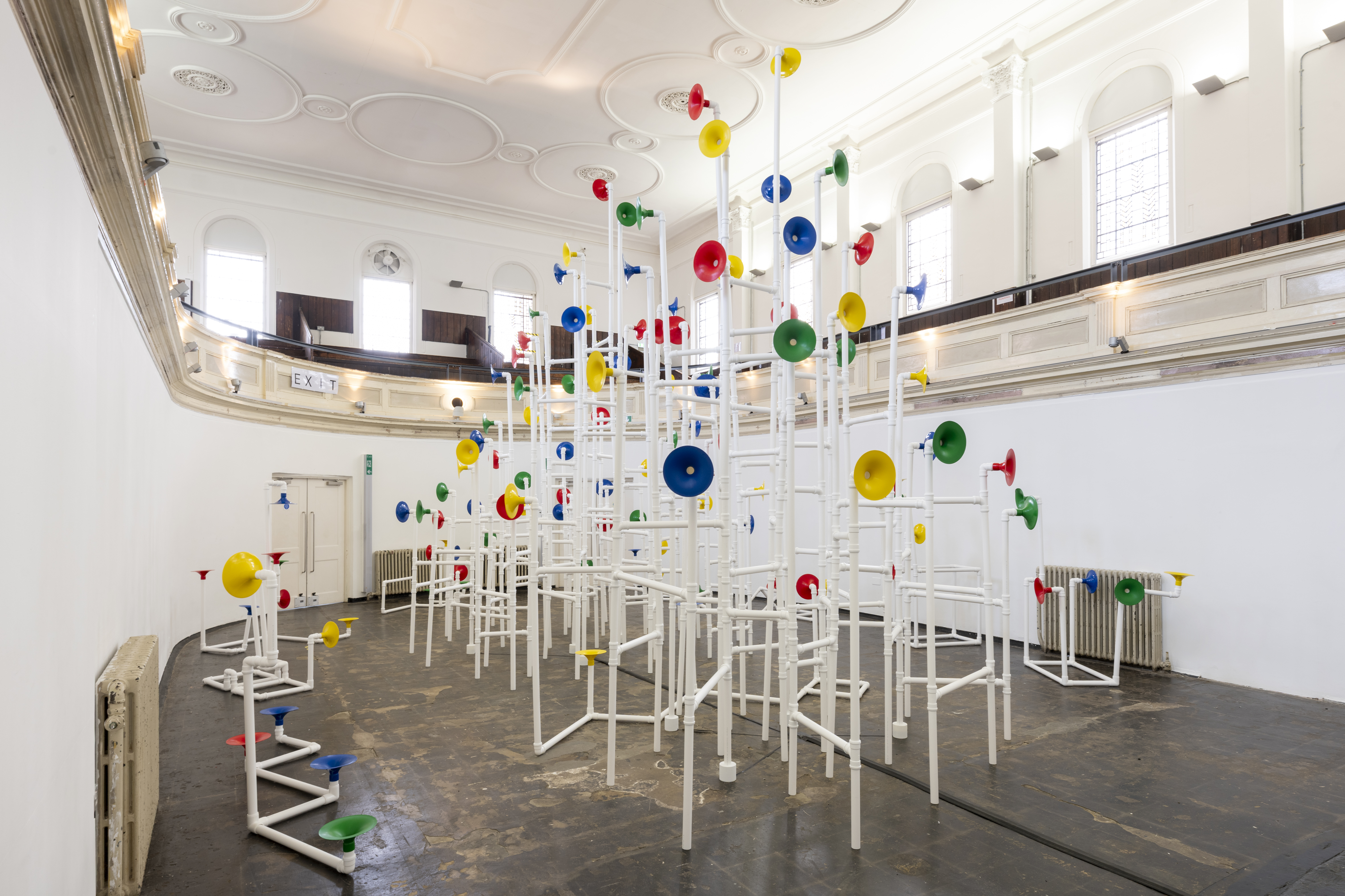 Installation in a former church made out of white pipes and colourful funnels