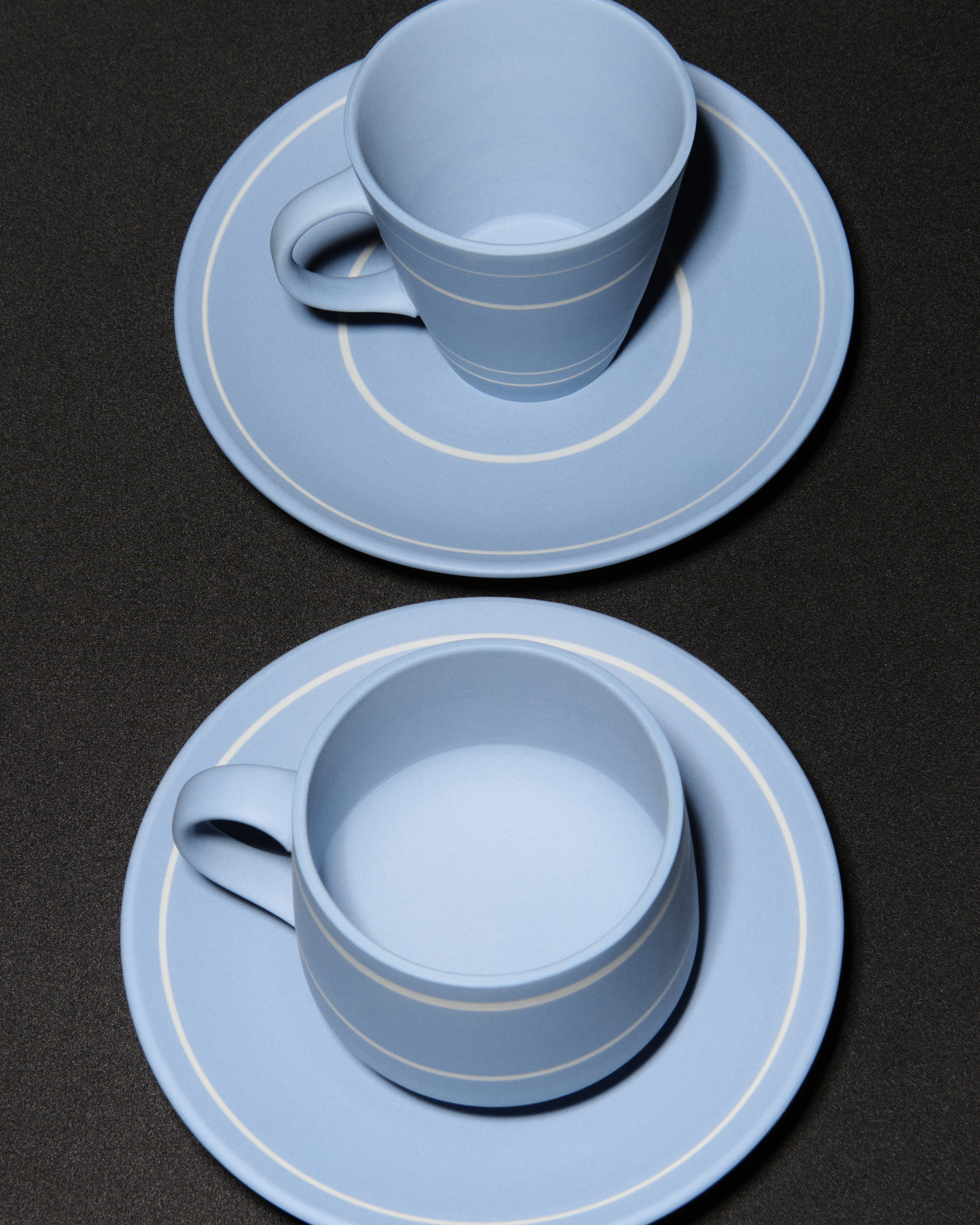 Blue cups with white horizontal lines, resting on blue plates with white lines around the border