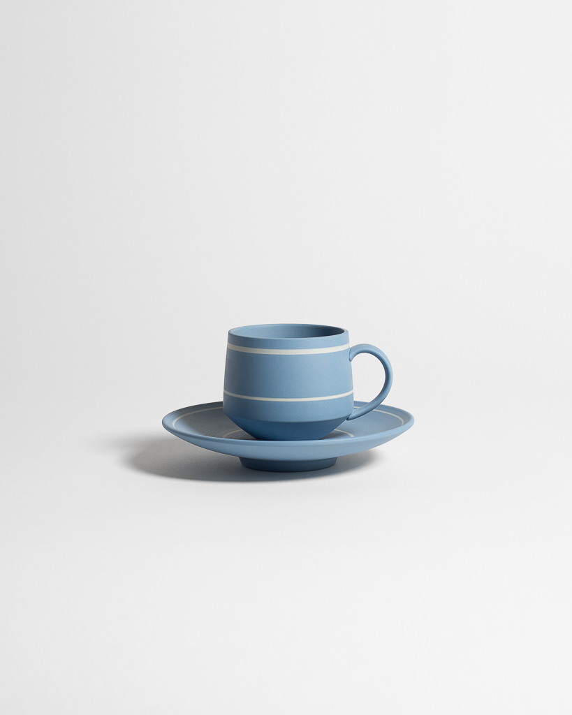 Blue cup with white horizontal lines, resting on round plate with a white line around its edge