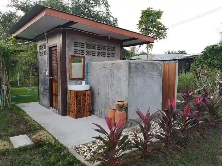 A rustic concrete outhouse with an outdoor sink