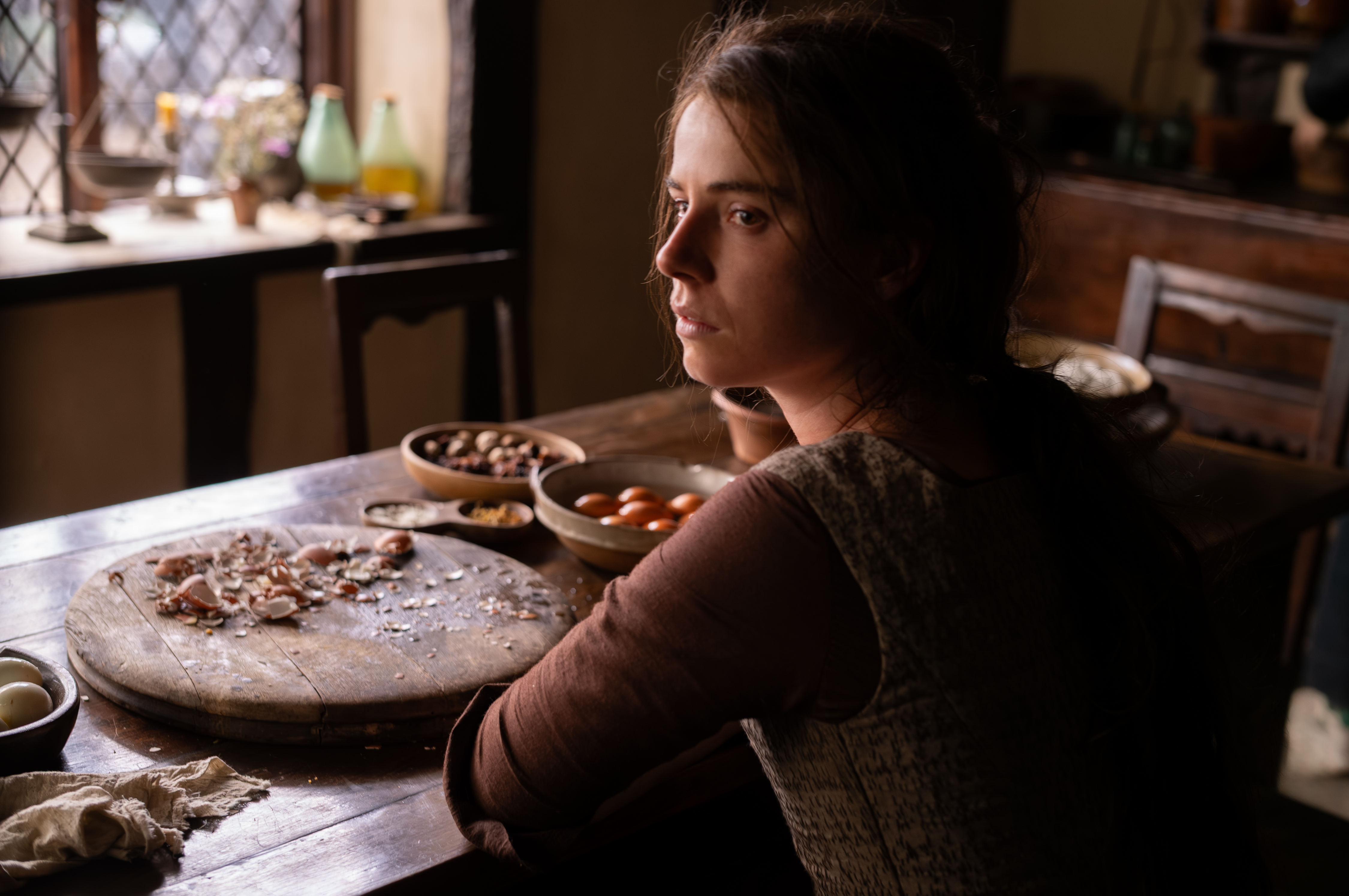 Actor Jessie Buckley as Agnes Shakespeare, seated at a kitchen table, in the film Hamnet