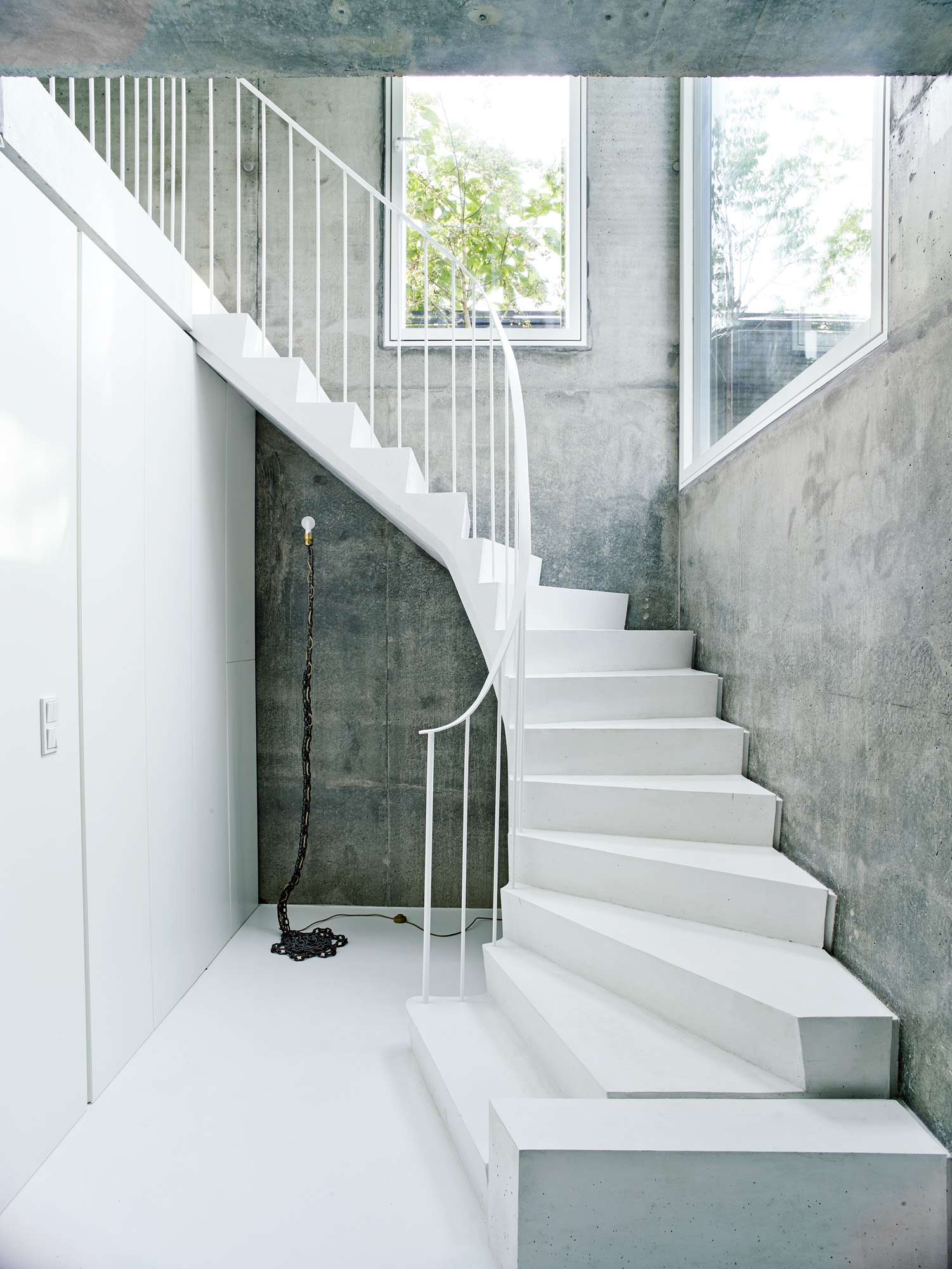 A white staircase curves around between two concrete walls