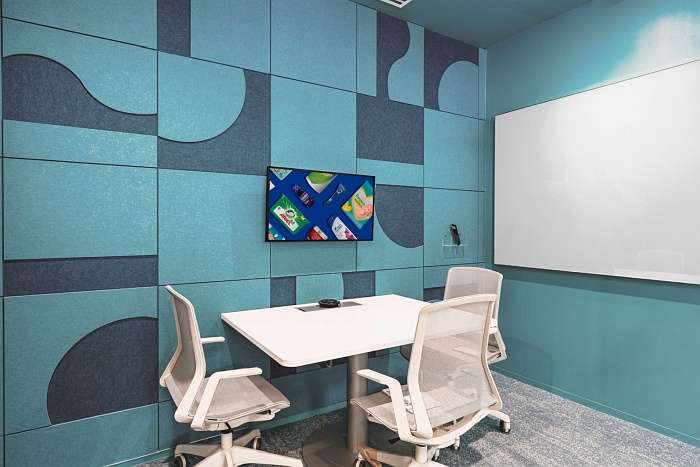 Small meeting room with blue acoustic wall panels and white task chairs.