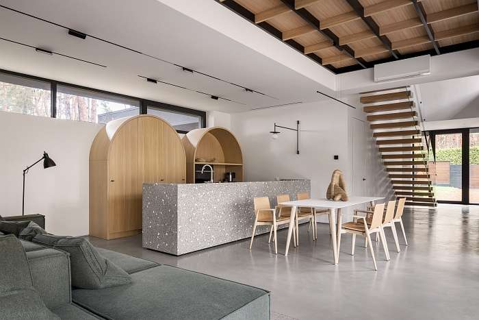 Kitchen with speckled stone island and curved wood cabinets in a black modern forest house.