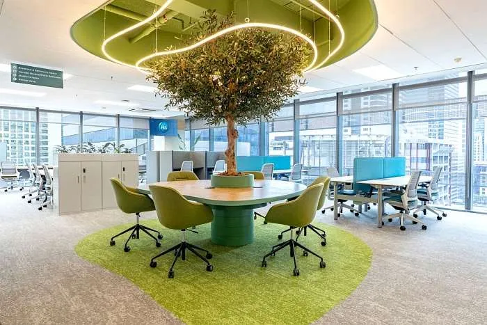 Central collaboration area with indoor tree and circular seating reflecting modern organic office ideas.