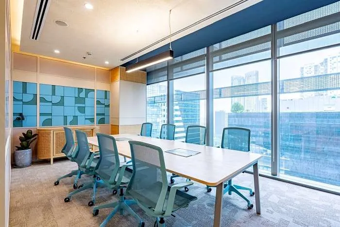 Glass-walled meeting room with turquoise chairs and natural light in a modern organic office in Manila.