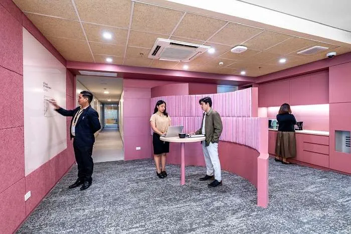 Pink-toned collaboration room with integrated cabinetry and informal meeting setup.