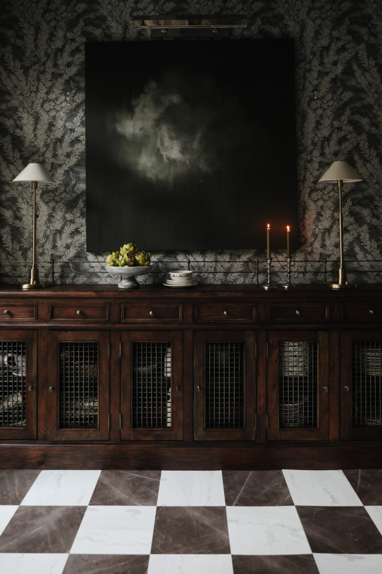 A vintage wooden sideboard in a moody traditional dining room with decorative items next to a bronze & white marble-look peel-and-stick floor.