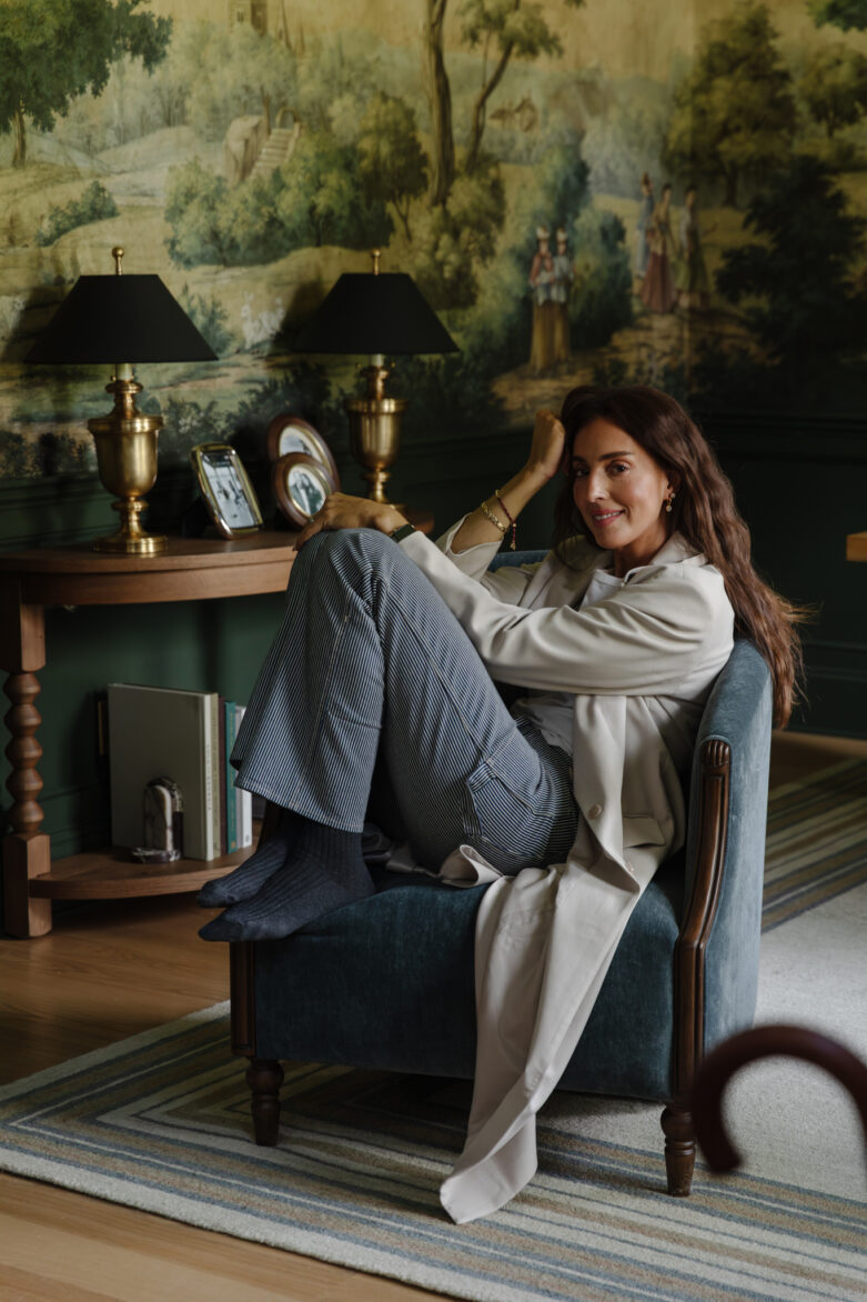 Julia Marcum relaxing in a stylish living room with vintage lamps, a mural wall, and comfortable armchair, showcasing home decor ideas.
