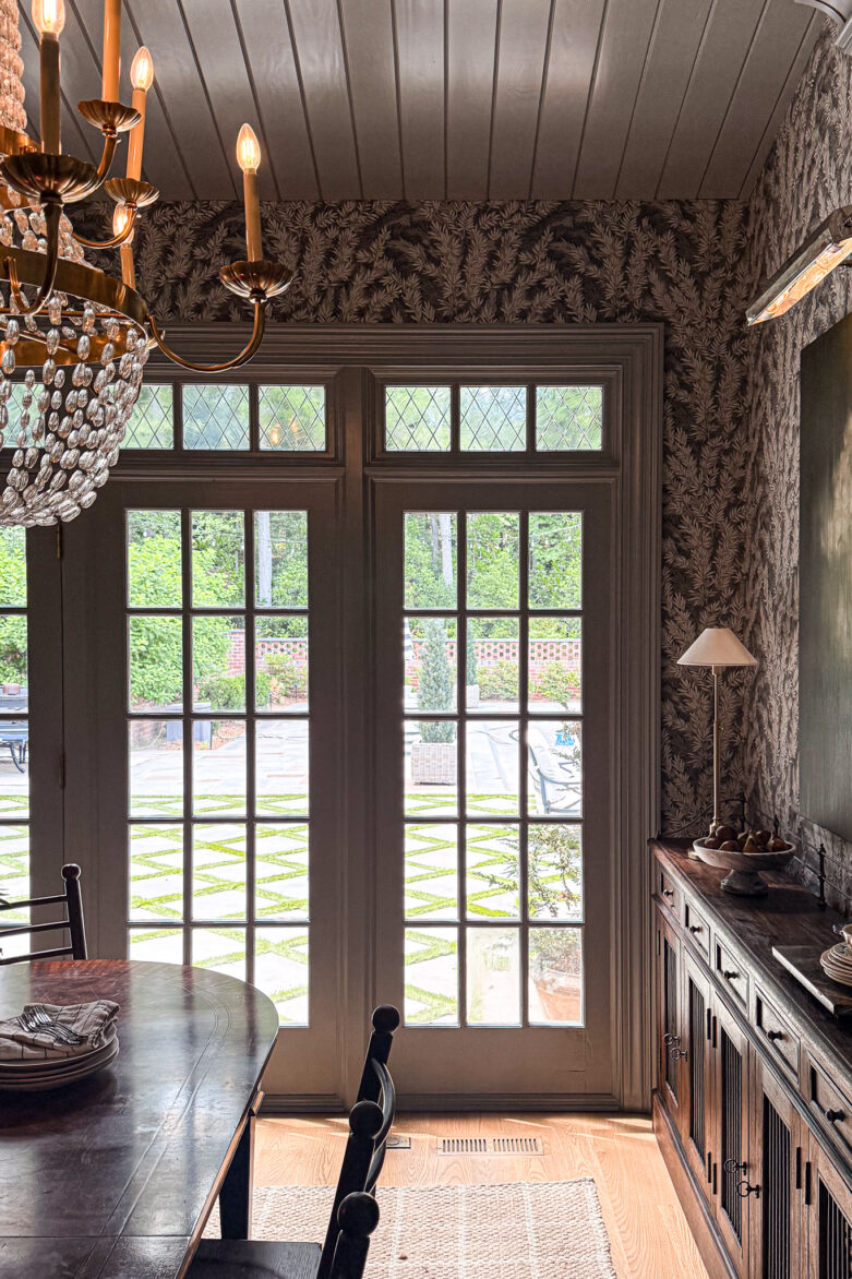 Elegant dining room featuring large glass doors, vintage wallpaper, and a classic chandelier. Perfect for family meals and entertaining guests in a stylish, inviting space.