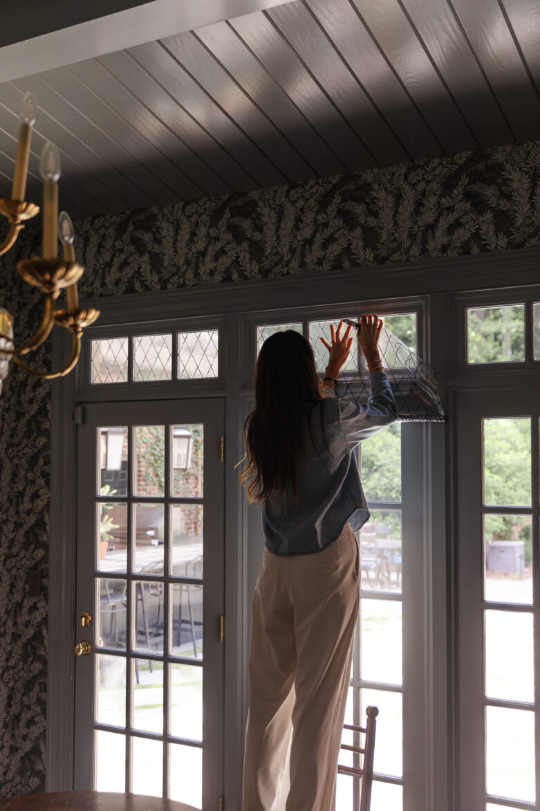 Woman cleaning large window in a modern, stylish home with natural light and elegant decor.