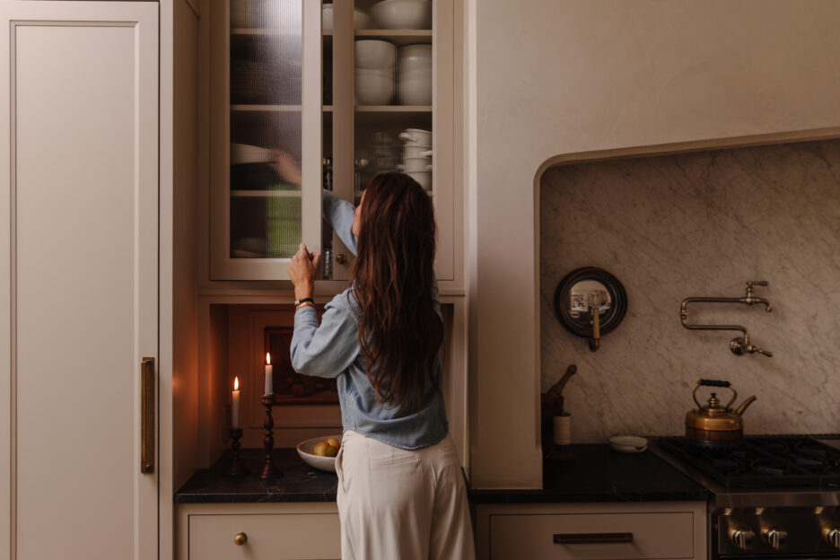 Julia Marcum organizing glassware in a modern kitchen cabinet with glass doors, showcasing stylish kitchen storage and decor.